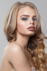 Naklejka premium Glamorous young blonde model with long wavy hair, makeup and clean skin on white background. Healthy woman portrait