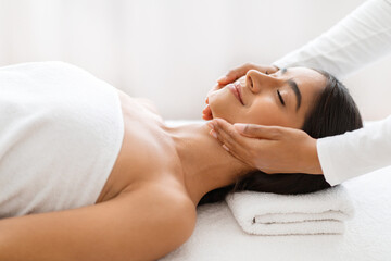 Fototapeta na wymiar Relaxed young indian woman enjoying face lifting massage in spa