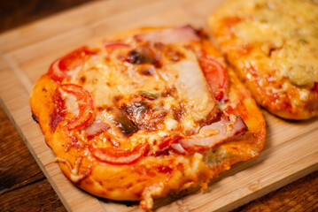 Mini Pizza Treats: Two delicious miniature pizzas topped with ham and cheese, artfully arranged on a wooden cutting surface