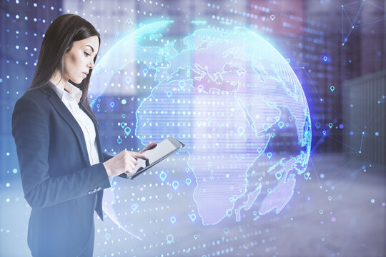 Young european businesswoman using tablet with glowing globe hologram with location pins on blurry office interior background. Elements of this image furnished by NASA. Marked location concept.