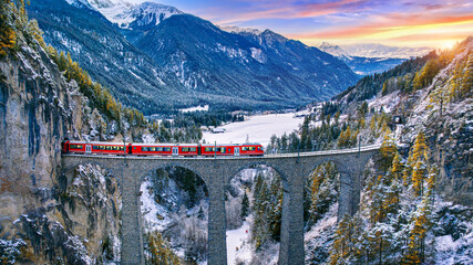 Aerial view of Train passing through famous mountain in Filisur, Switzerland. Landwasser Viaduct world heritage with train express in Swiss Alps snow winter scenery. - obrazy, fototapety, plakaty
