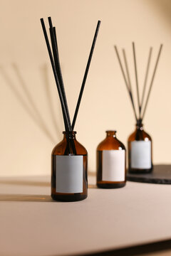 Focus on One Organic Essential Oil Diffuser Bottle with Wooden Sticks on a Background of 2 blurred bottles, Seamless Beige Brown Backdrop, Ready for Custom Labeling