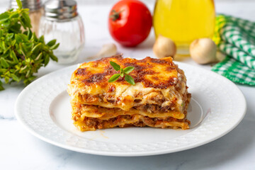 Portion of ground beef lasagna topped with melted cheese and garnished with fresh parsley served on...