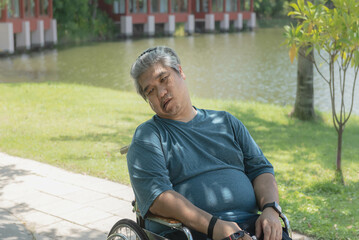 Middle-aged Asian man sitting in a wheelchair The mouth is distorted due to nervous system illness...