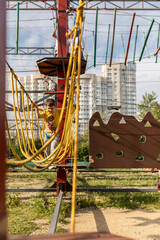A happy child, a healthy boy enjoys the activity in the climbing adventure park on a summer day. Overcomes obstacles