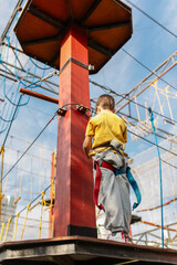 A happy child, a healthy boy enjoys the activity in the climbing adventure park on a summer day. Overcomes obstacles