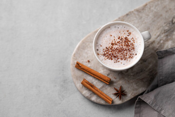 White mug of hot cocoa or chocolate with whipped cream, cinnamon sticks and star anise on a gray...