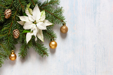 Christmas decor with fir-tree branches, white poinsettia, golden colored Christmas balls and cones on the light blue background. Top view, close up, flat lay