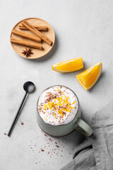 Flat lay of a mug of hot chocolate with whipped cream and orange zest on a light background with a...
