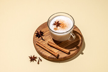 Traditional Indian masala chai latte in a glass cup. Hot drink with milk, spices and herbs on a wooden board on a yellow  background