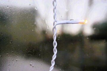 Wei&szlig;e kleine Lichterkette vor feuchter Glasscheibe mit Regentropfenmuster bei Regen im Winter
