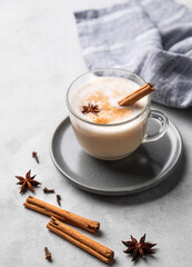 Obraz na płótnie Canvas Traditional Indian masala chai latte in a glass cup. Hot drink with milk, spices and herbs on a plate on a light background