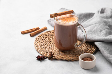 Glass mug with hot chocolate and milk foam on a light background with cinnamon sticks, anise star...