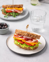 Two toast club sandwiches made of grain bread with cheddar cheese and bacon stuffed with tomatoes, lettuce on a light background