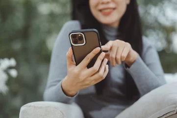 Photo sur Aluminium brossé Magasin de musique Happy young asian woman relax on comfortable couch at home texting messaging on smartphone, smiling girl use cellphone chatting, browse wireless internet on gadget, shopping online from home