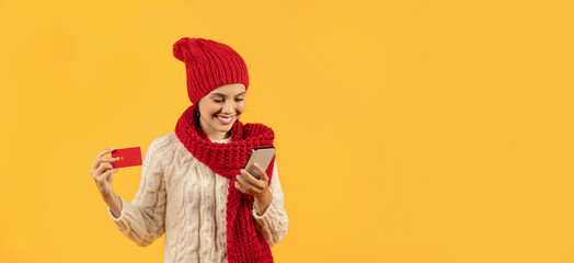 lady in winter hat using smartphone and credit card, studio