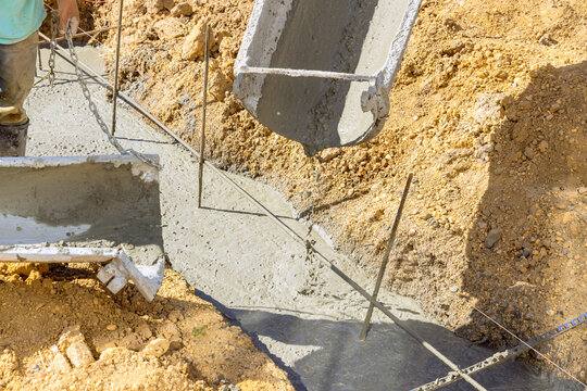 An individual laying cement pouring concrete in trenches for foundation of house
