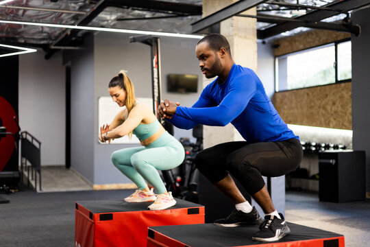 A couple of young people of different ethnicities are jumping on a plyometric box inside a gym. Jump concept. Plyometric jump to develop explosive strength and aerobic power. Functional exercise.