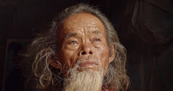 Asian male farmer who is a poor elderly man with long hair and a long beard, work as a farm worker and live in a worker's house in the countryside, looking up at the sky.