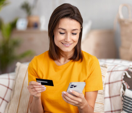 Woman is doing online purchases sitting on the sofa in the living room at home, shopping concept