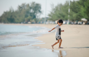 4 years boy wearing sunglasses is playing on a sandy beach near the sea.