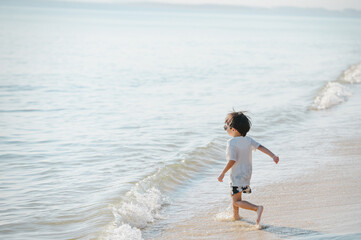 4 years boy wearing sunglasses is playing on a sandy beach near the sea.