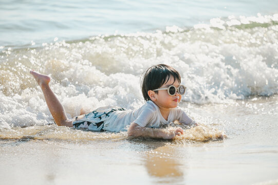 4 years boy wearing sunglasses is playing on a sandy beach near the sea.
