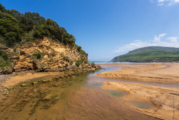 Rio Barbadun under a blue sky flowing into the Bay of Biscay at La Arena beach in Pobeña, Basque country, Spain