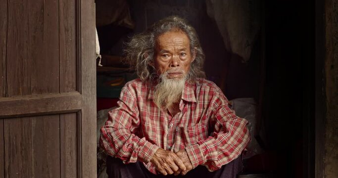 Asian male farmer who is a poor elderly man with long hair and a long beard, work as a farm worker and live in a worker's house in the countryside, looking at the tourists.