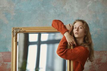 Dreamy young girl leaning on mirror in golden antique frame