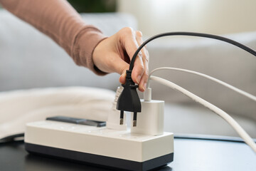 Closed up hand of woman plugged in, unplugged electricity cord cable on socket on table for energy saving, electric power on plate outlet, control expense electrical appliances, environment concept. - obrazy, fototapety, plakaty