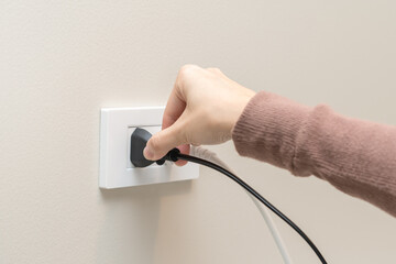 Hand of woman plugged in, unplugged electricity cord cable at home, put on or remove electric plug cable in socket on wall outlet for saving, control power electrical energy, eco environment concept.