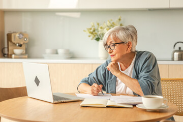 Online education courses webinar concept. Middle aged senior woman using laptop computer writing notes. Focused mature old woman enjoying studying online from home written records doing online work - obrazy, fototapety, plakaty