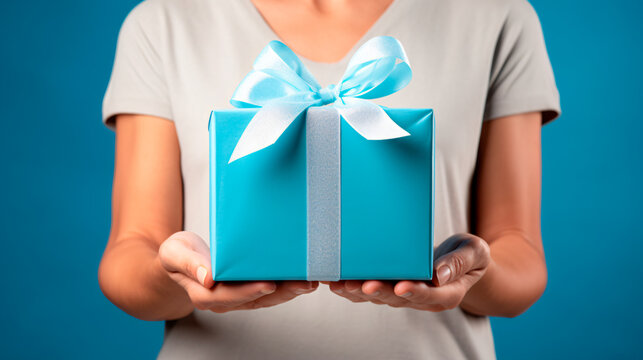 plano detalle de manos sosteniendo una caja de regalos color azul en vista frontal con un mo&ntilde;o
