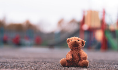 Lost teddy bear toy lying on playground floor in gloomy day,Lonely and sad brown bear doll lied down alone in the park, Lost toy or Loneliness concept,International missing Children day - obrazy, fototapety, plakaty