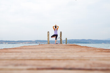 woman makes yoga on the wooden pier of a lake
