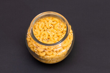 Uncooked Chifferi Rigati Pasta in Glass Jar on Black Background. Fat and Unhealthy Food. Classic Dry Macaroni. Italian Culture and Cuisine. Raw Pasta
