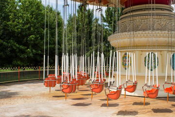 Retro carousel on chains not working with empty seats on a sunny summer day at an amusement park in...
