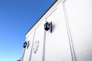 Two black street lamps hanging on a white facade. A blue sky in the background.