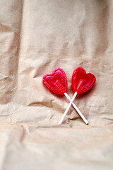 Two red heart-shaped lollipops together on a cardboard background.