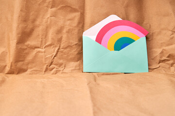 Green envelope with a rainbow-shaped card on a cardboard textured background.
