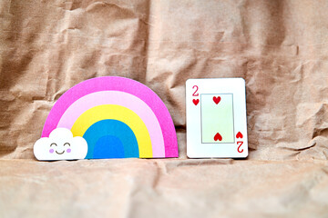 Two of hearts poker card with a rainbow shaped card on a cardboard background.