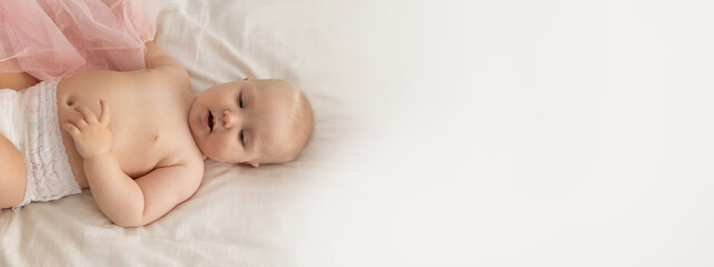 A young toddler in diapers rests on a light sheet with a copy space