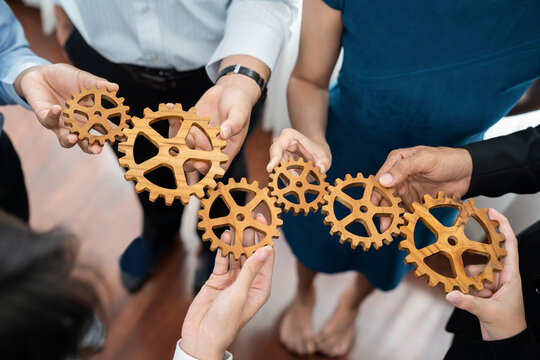 Office worker holding cog wheel as unity and teamwork in corporate workplace concept. Diverse colleague business people showing symbol of visionary system and mechanism for business success. Concord