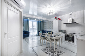 Kitchen and dining room in the interior of luxury apartments. A table with an elegant .setting, a white kitchen set. Beautiful floor tile pattern.