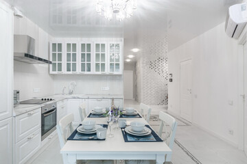 Stylish interior of the kitchen, decorated in white. A table with an elegant setting. .Beautiful chandelier over the dining table.