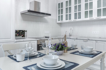 A table with an elegant setting and cute Christmas decorations, in the interior of a .modern kitchen with white furniture.