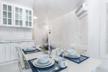 The kitchen is decorated in white. Kitchen set with built-in appliances. Elegant table .setting.