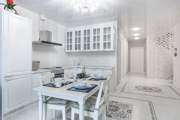 The interior of the kitchen with an exquisite design. A table with an elegant setting. .The room with furniture is decorated in white.