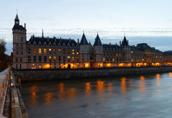 Conciergerie Building in Paris, France at night with lights reflection in the Seine River water .